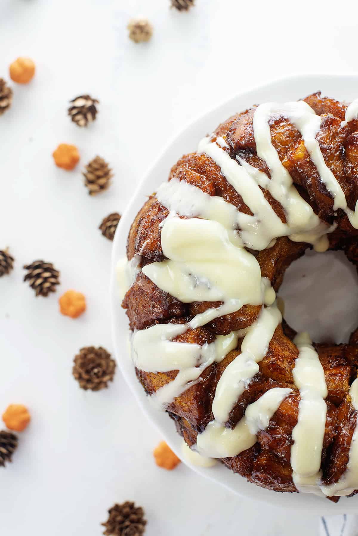 Monkey bread on white cake plate surrounded by pinecones and small pumpkins.