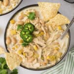 Bowl full of white chicken chili topped with tortilla chips and sliced jalapeno.