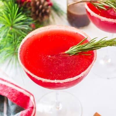 Cranberry cocktail in glass with sprig of rosemary.