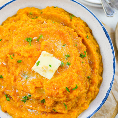 Mashed sweet potatoes in bowl with butter on top.