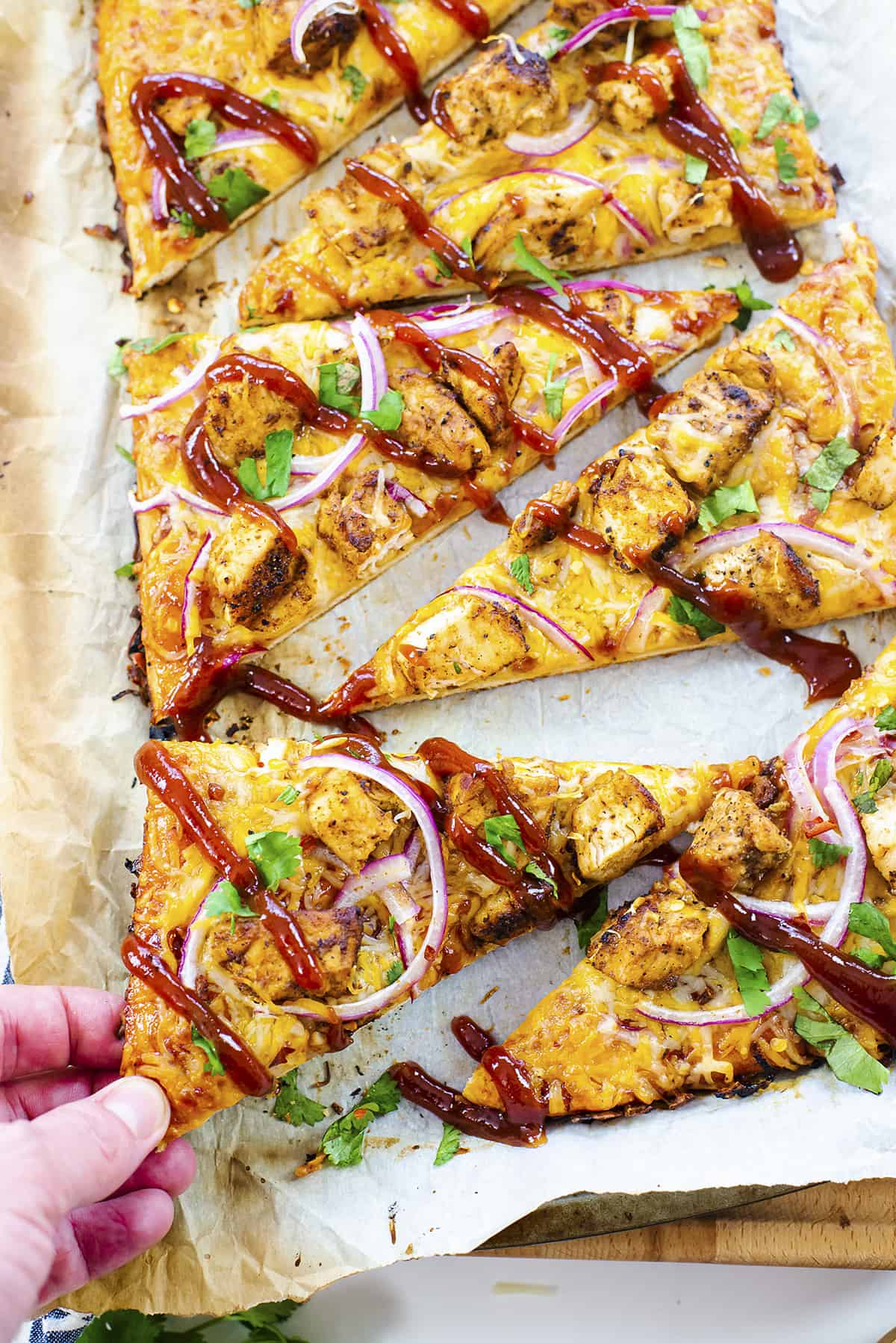 Hand grabbing a slice of BBQ chicken flatbread.