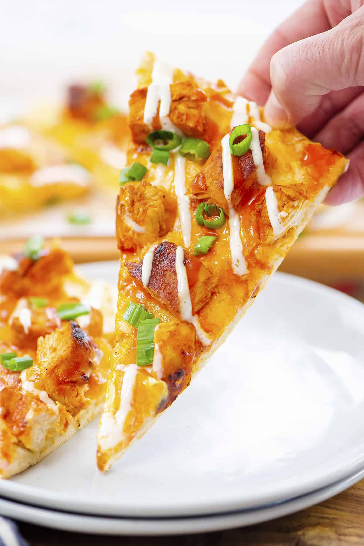 Hand holding a slice of buffalo chicken flatbread.