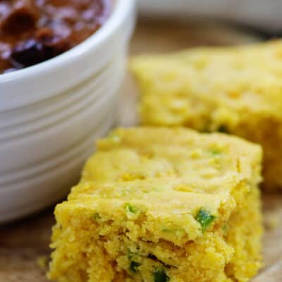 Slice of jalapeno cheddar cornbread next to bowl of chili.