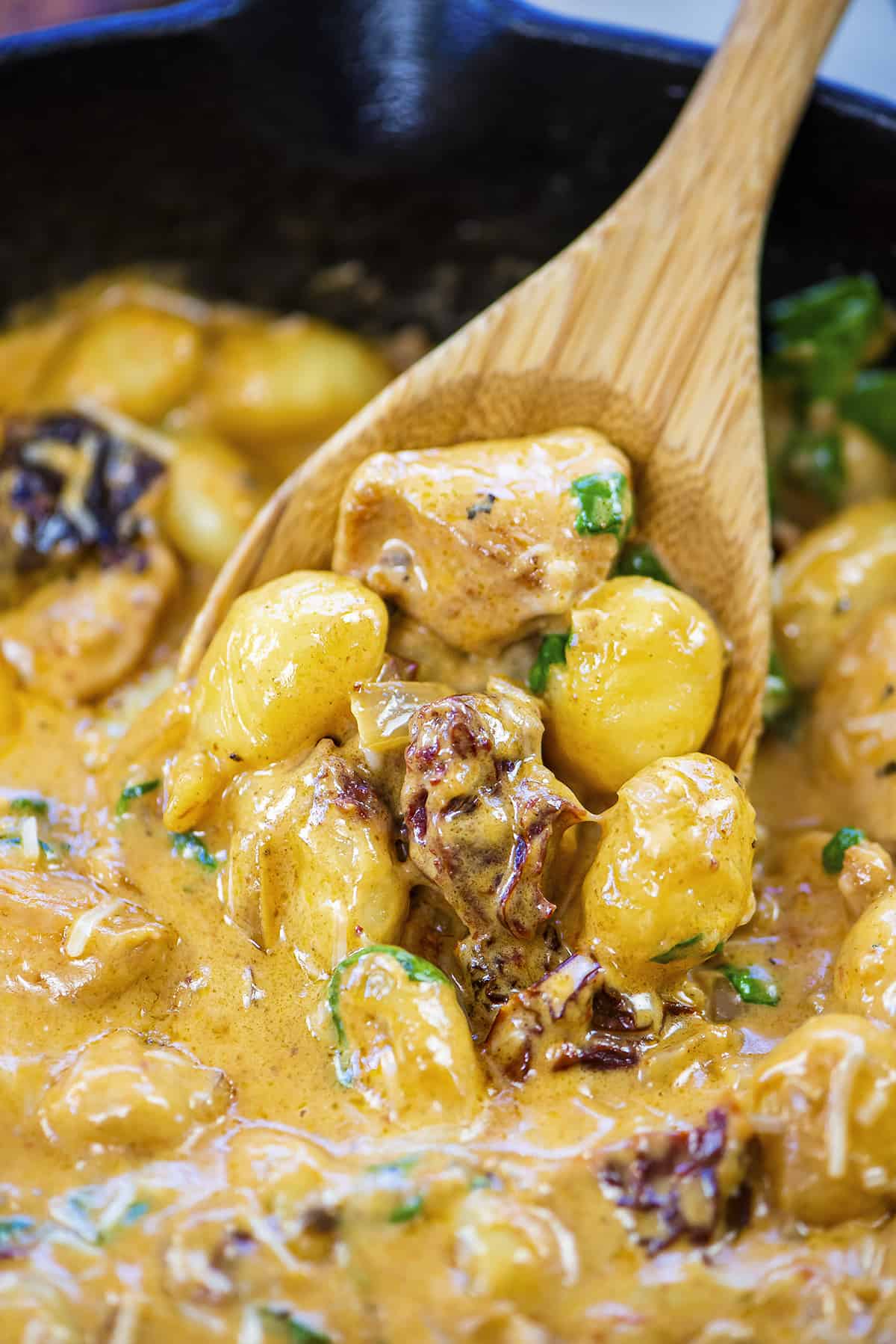 Wooden spoon loaded with chicken and gnocchi in cream sauce.