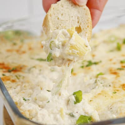 Hand dipping a piece of bread in artichoke crab dip.
