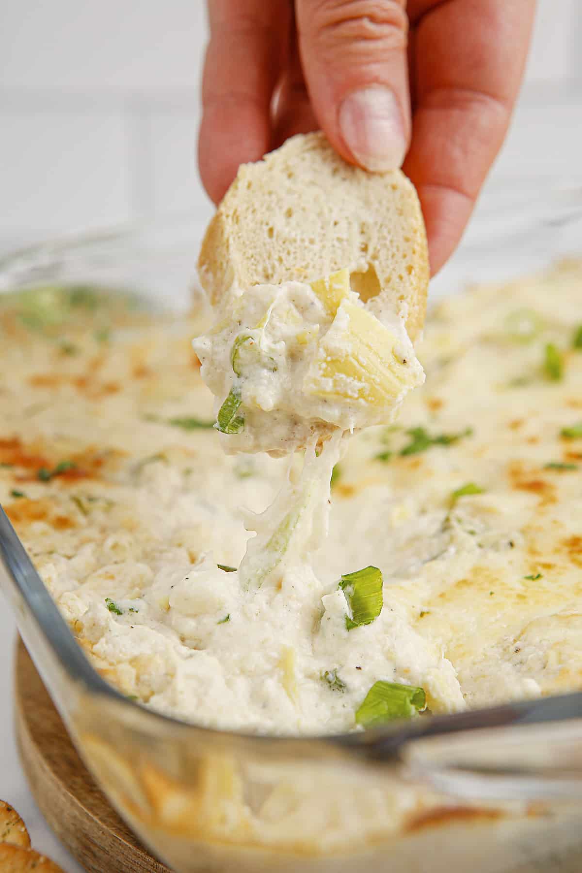 Hand dipping a piece of bread in artichoke crab dip.