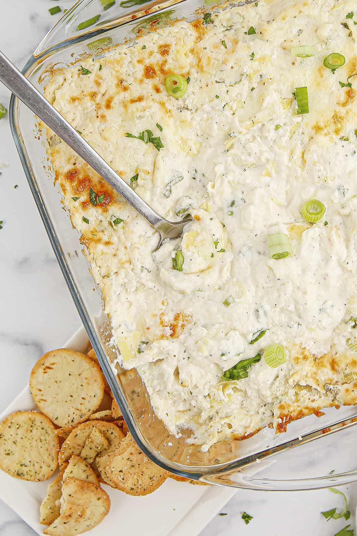 Cheesy artichoke dip with crab in glass baking dish.