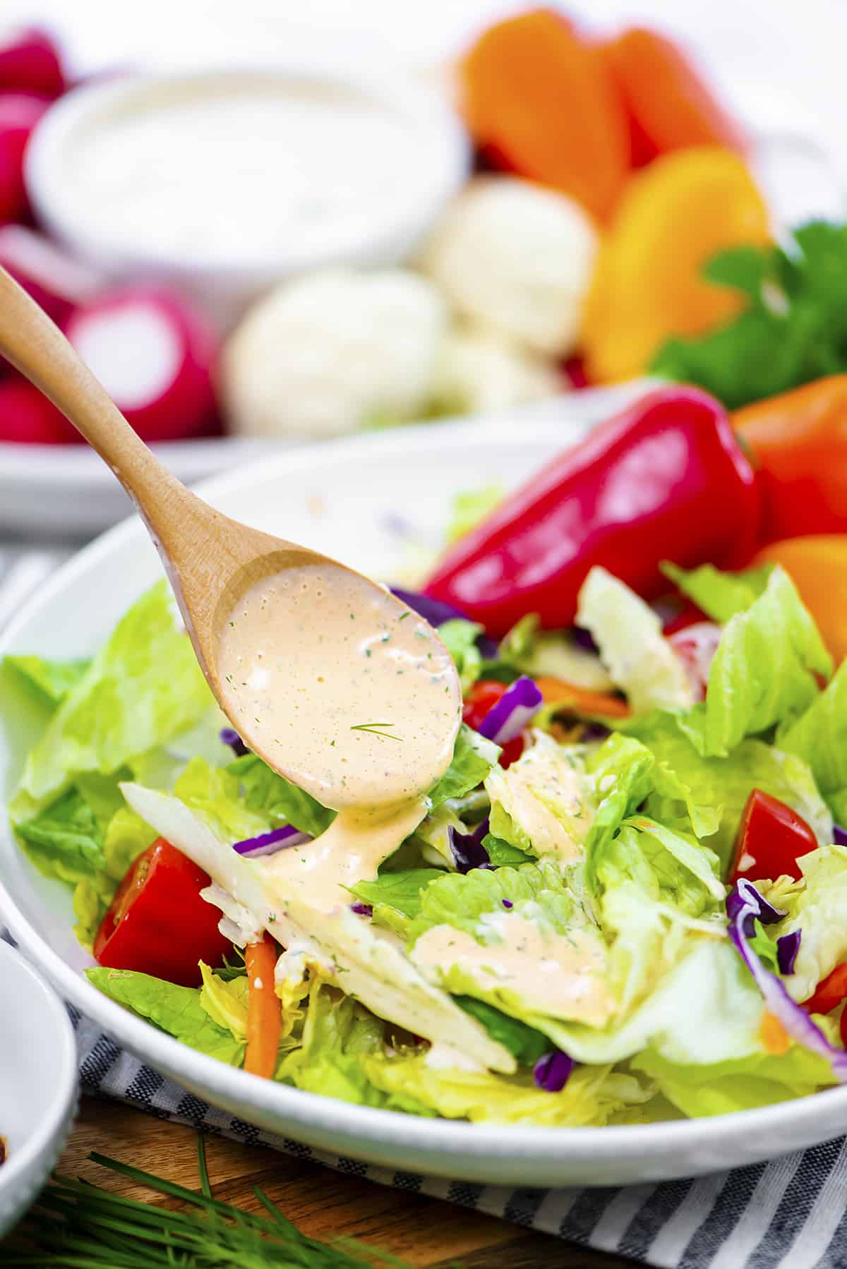 Dressing being drizzled over green salad.