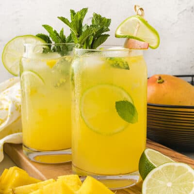 Mango mojitos in tall glasses next to basket of fruit.