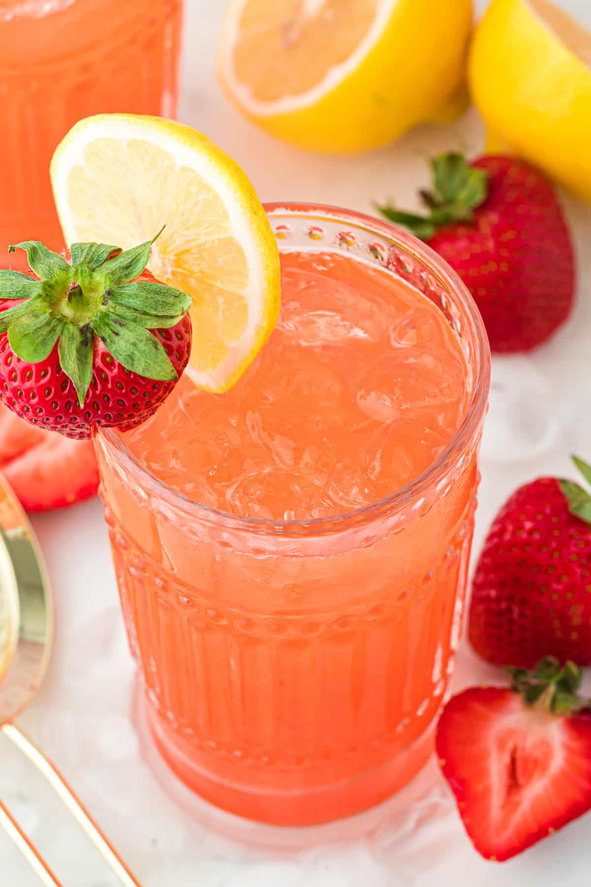 Glass of strawberry lemonade vodka with strawberry and lemon on the rim.