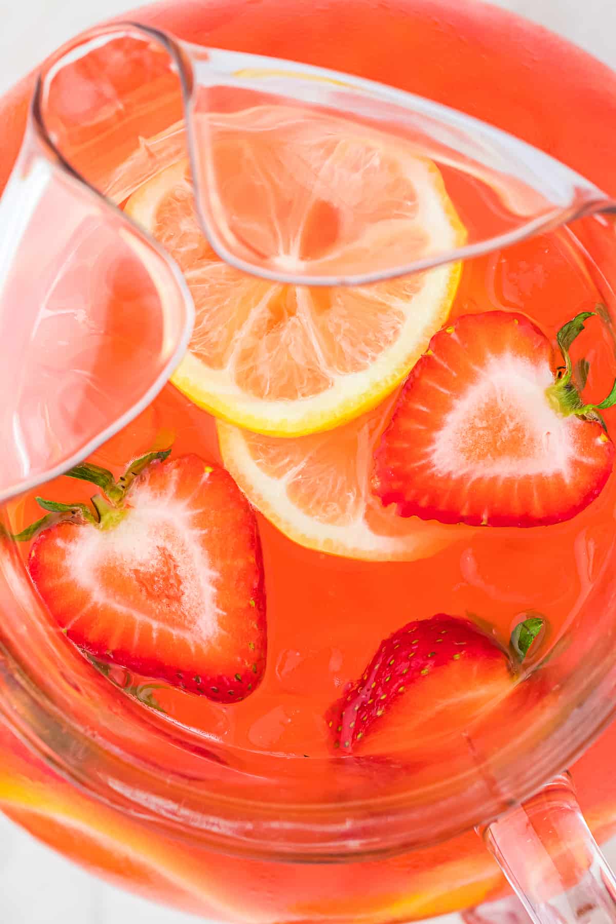 Overhead view of strawberries and lemons floating in a pitcher full of strawberry lemonade vodka.