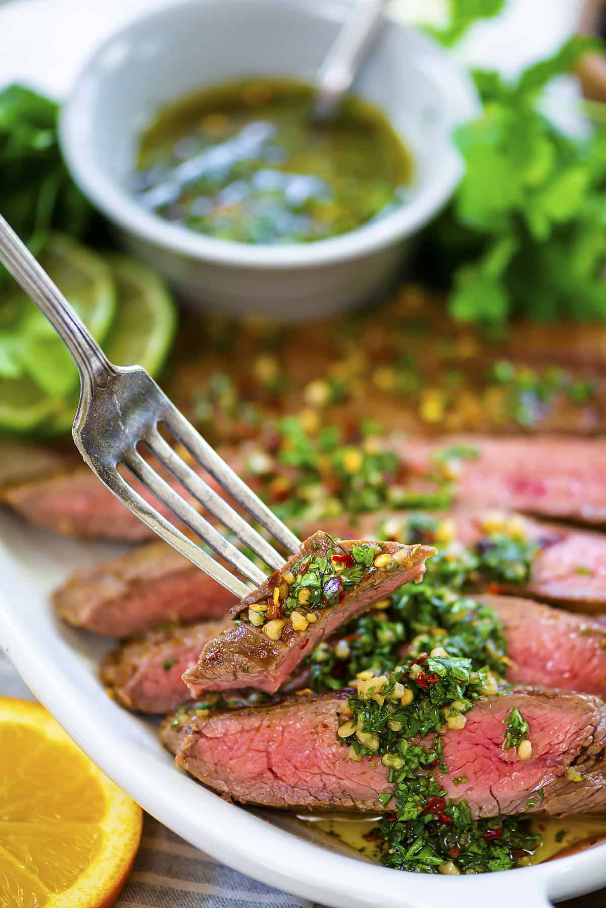 Fork pulling away a bite of flank steak with chimichurri sauce.