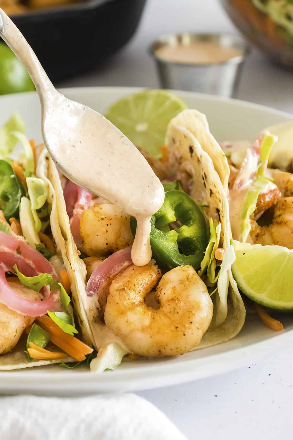 Chipotle sauce being drizzled over shrimp tacos.