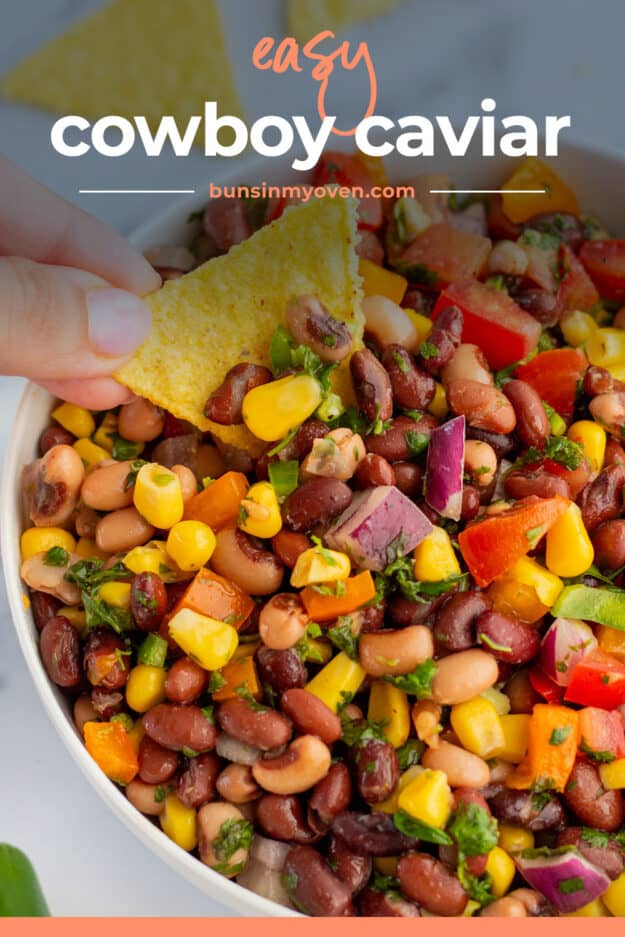 Hand dipping a tortilla chip into bean dip.