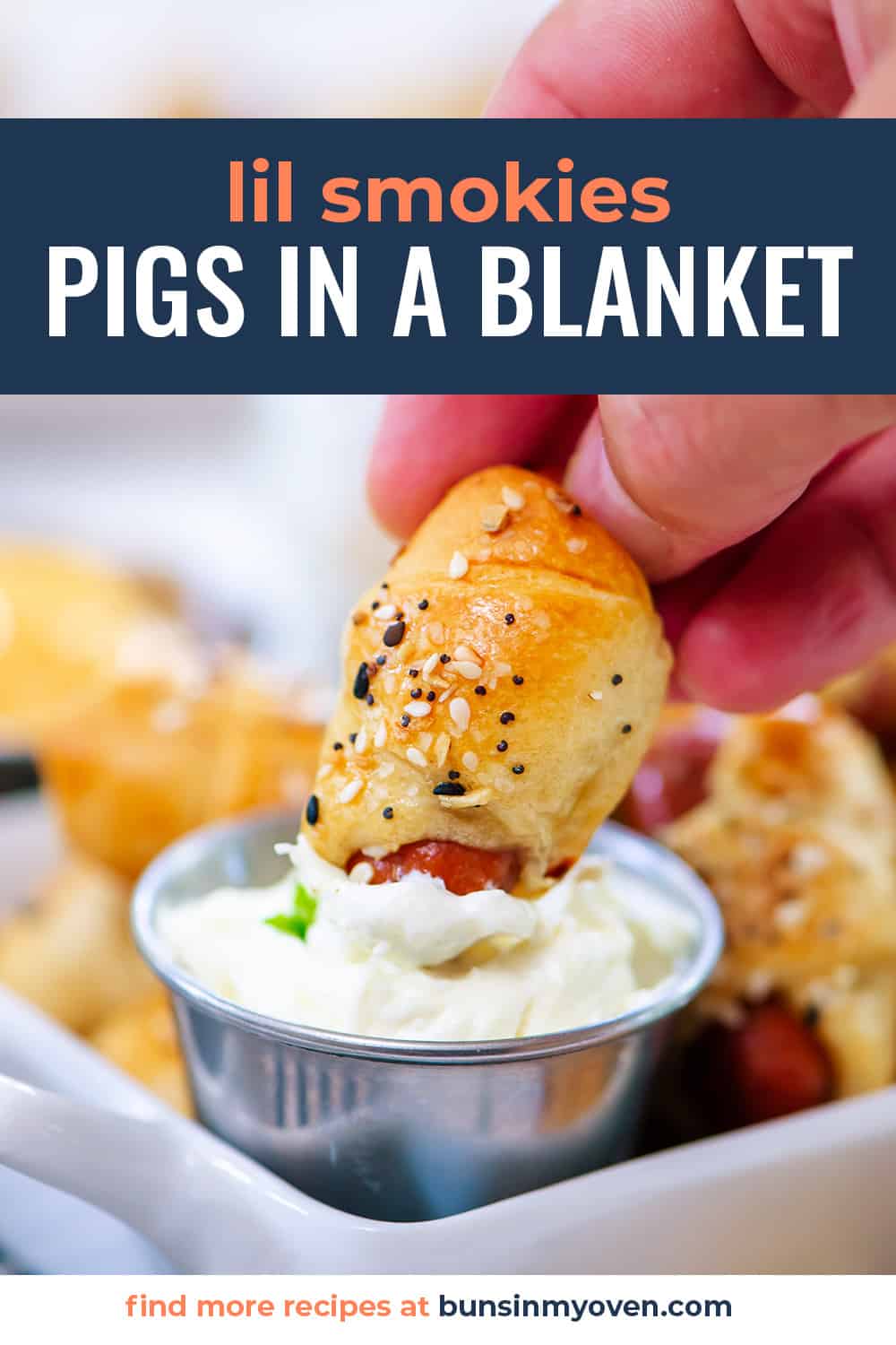 Hand dipping a pig in a blanket in cream cheese.