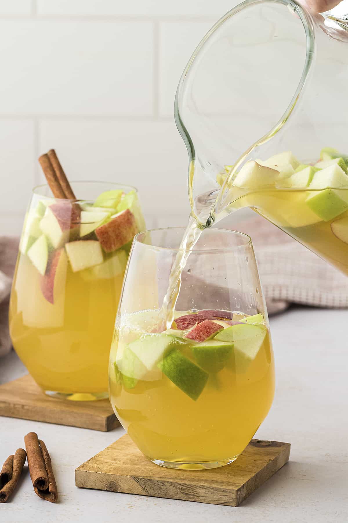Caramel apple sangria being poured from pitcher into stemless wine glass.