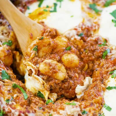 Baked gnocchi on wooden spoon in skillet.