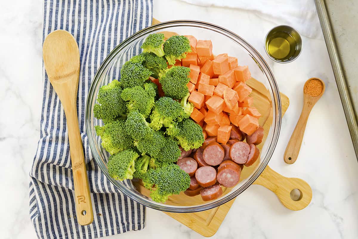 Ingredients for sheet pan sausage and veggies in glass mixing bowl.