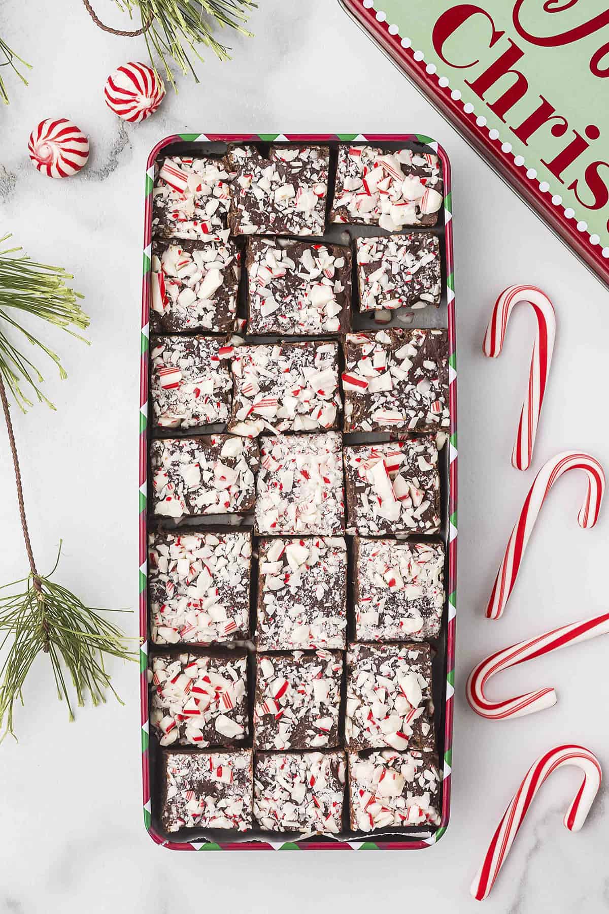 Peppermint fudge in Christmas tin surrounded by candy canes.