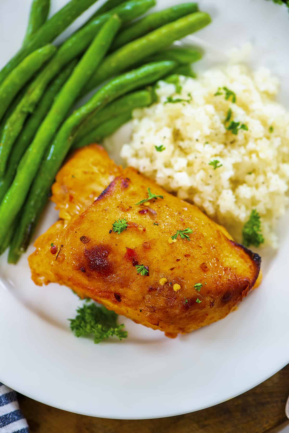 Overhead view of harissa chicken thighs on plate with cauliflower and green beans.