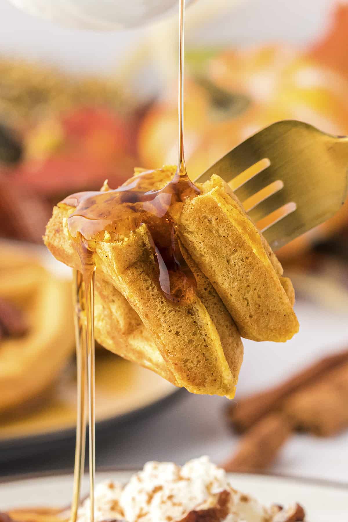 Bite of waffle on fork with syrup being drizzled over teh top.