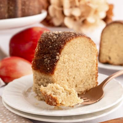 Slice of apple cider cake on white plate with fork.