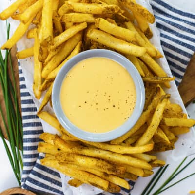 Bowl of cheese sauce surrounded by french fries.