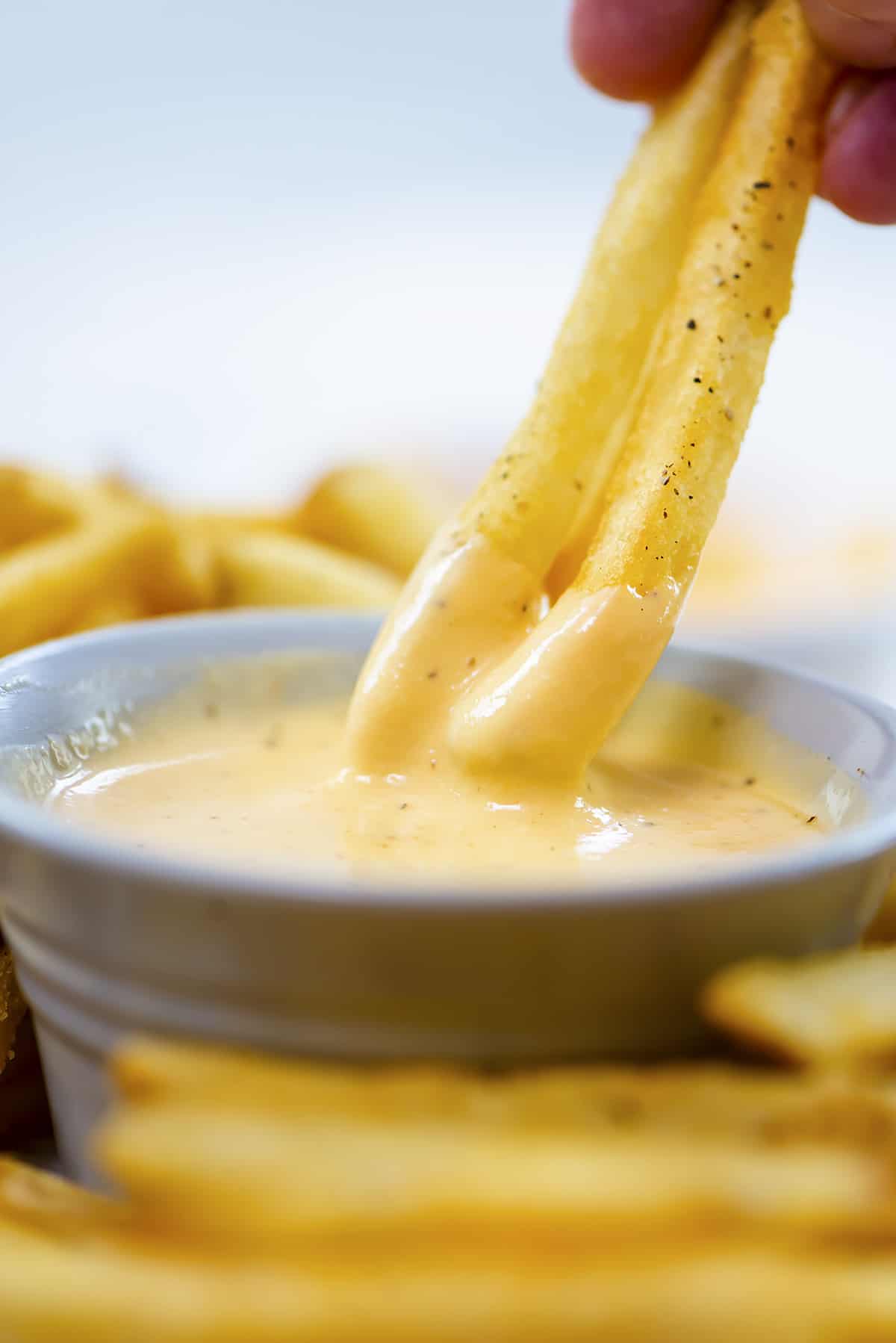 French fries being dipped in homemade cheese sauce.