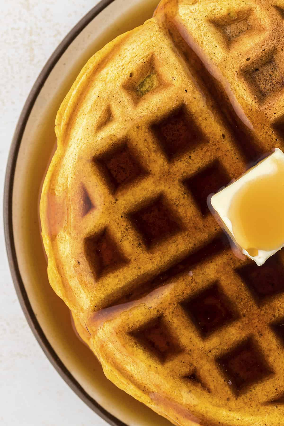 Overhead view of pumpkin waffle topped with butter and syrup.