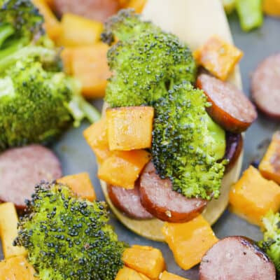 Sheet pan sausage and veggies on wooden spoon.