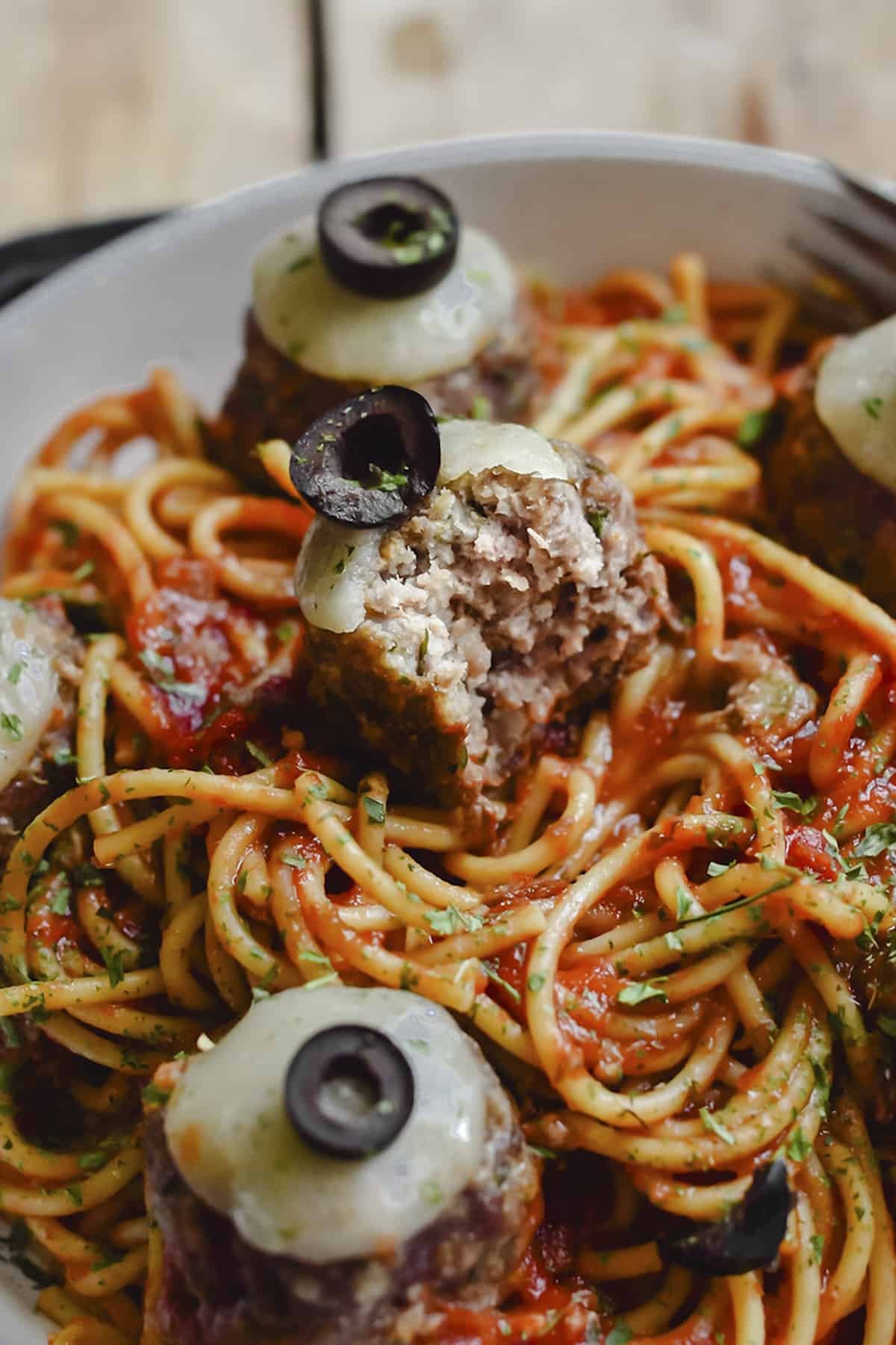 Spaghetti and meatballs topped with cheese and black olives.