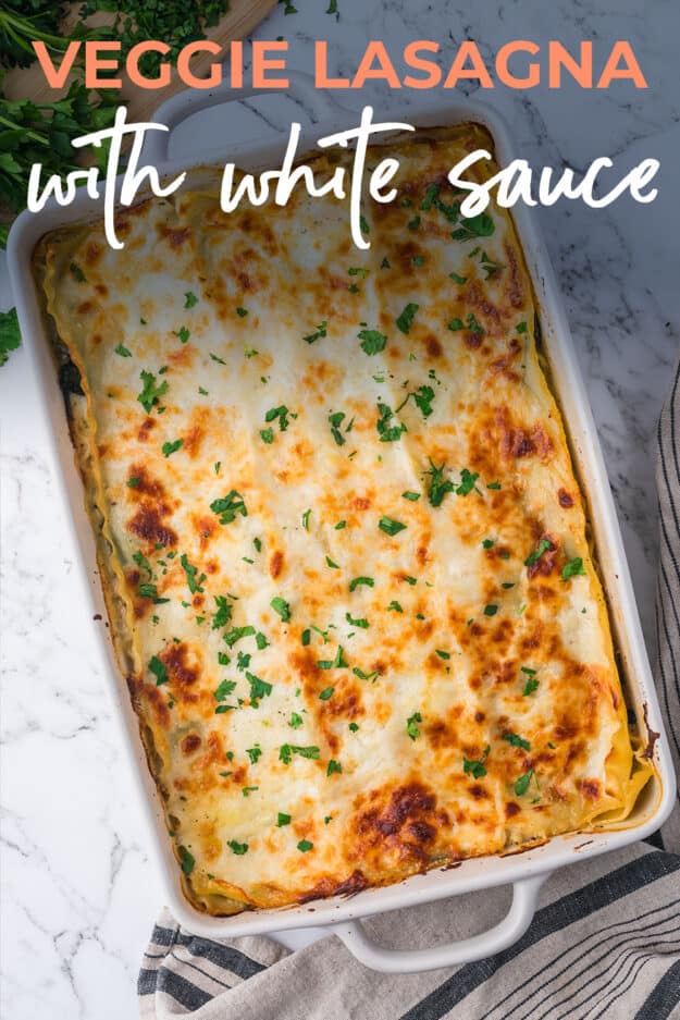 Vegetable lasagna with white sauce in white baking dish.