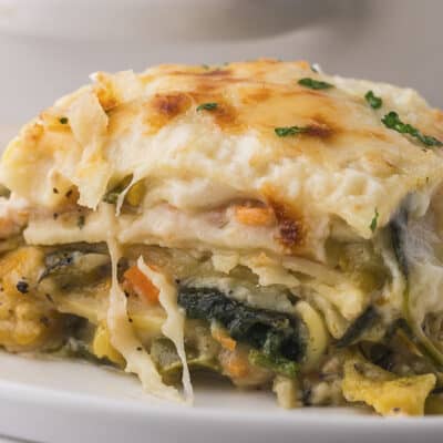Slice of vegetable lasagna with white sauce on small white plate.