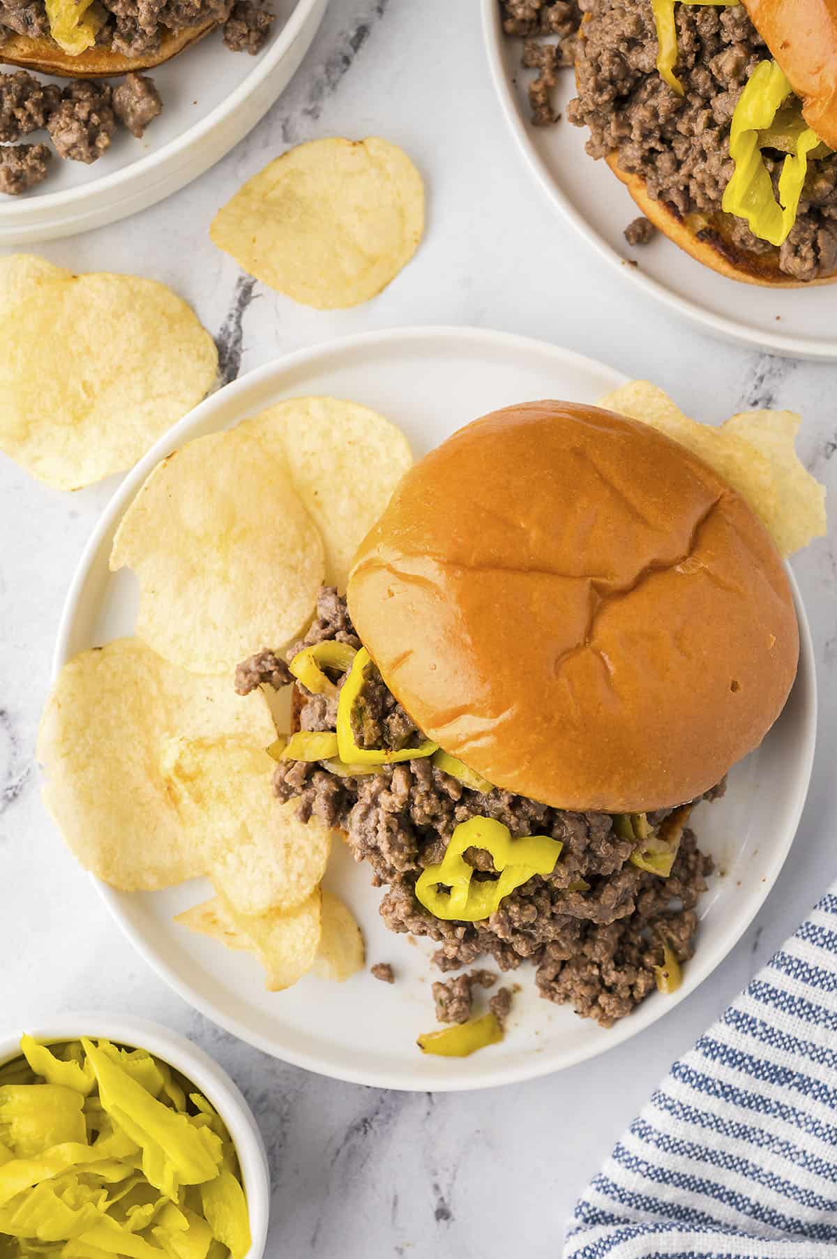 Overhead view of sloppy joe sandwich on white plate with chips.