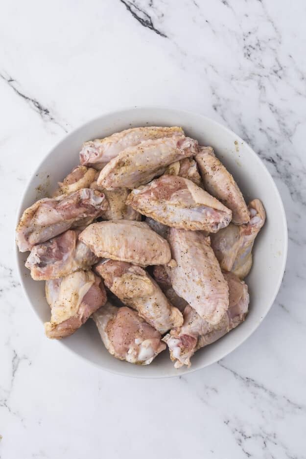 Seasoned chicken wings in glass mixing bowl.