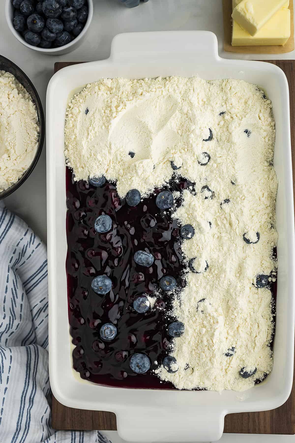Cake mix sprinkled over half of a blueberry dump cake.