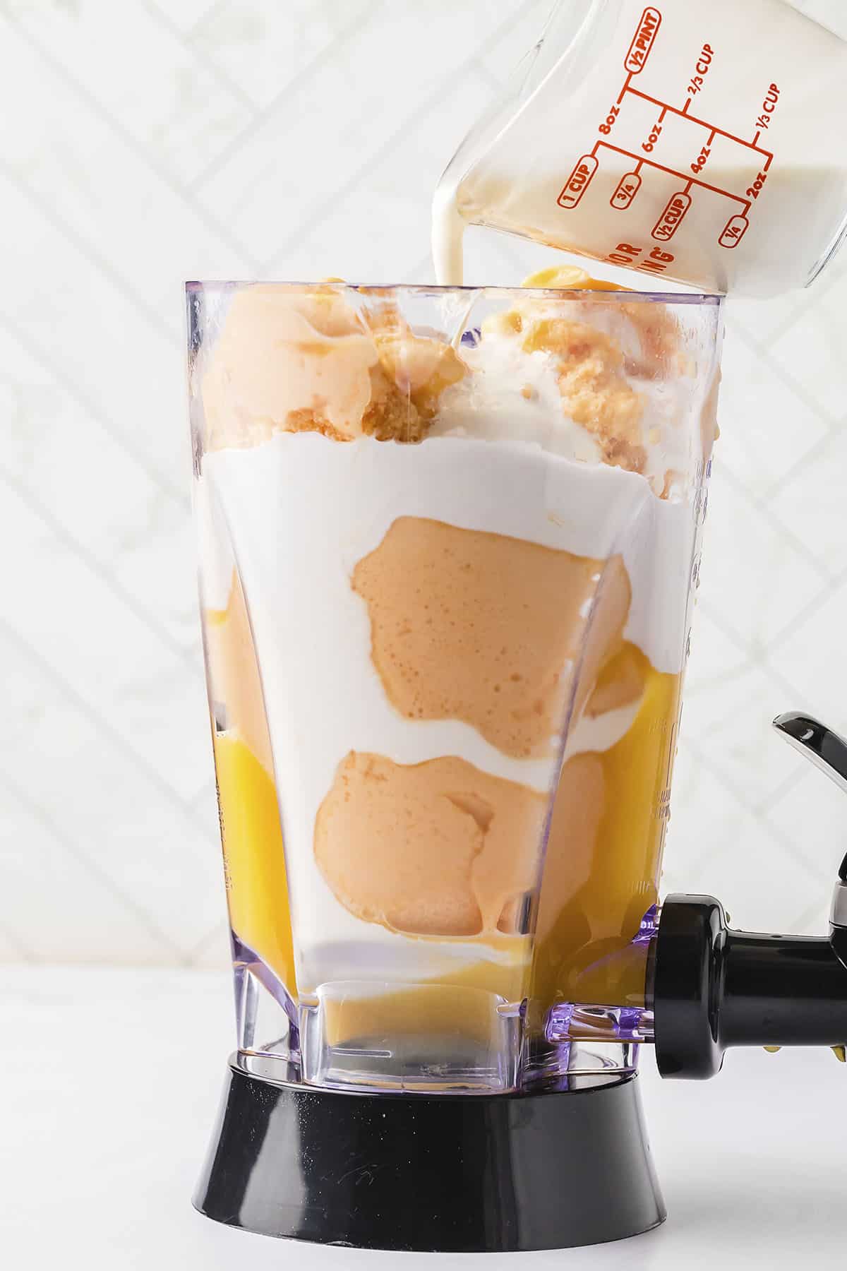 Orange creamsicle ingredients being poured into blender.