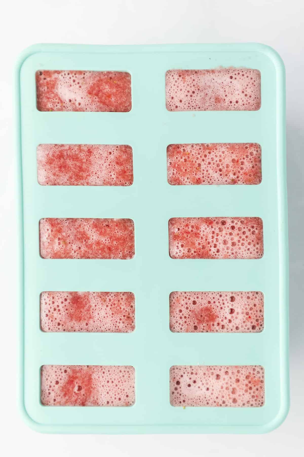 Strawberry popsicle mixture poured into popsicle mold.