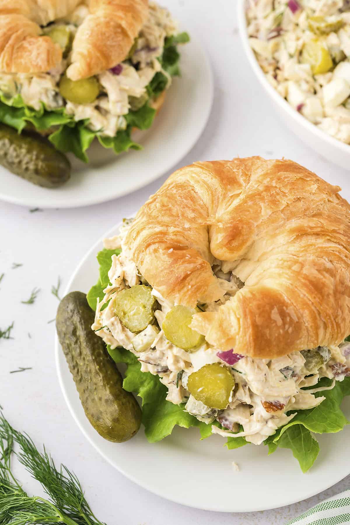 Chicken salad with pickles on croissant on small plate.