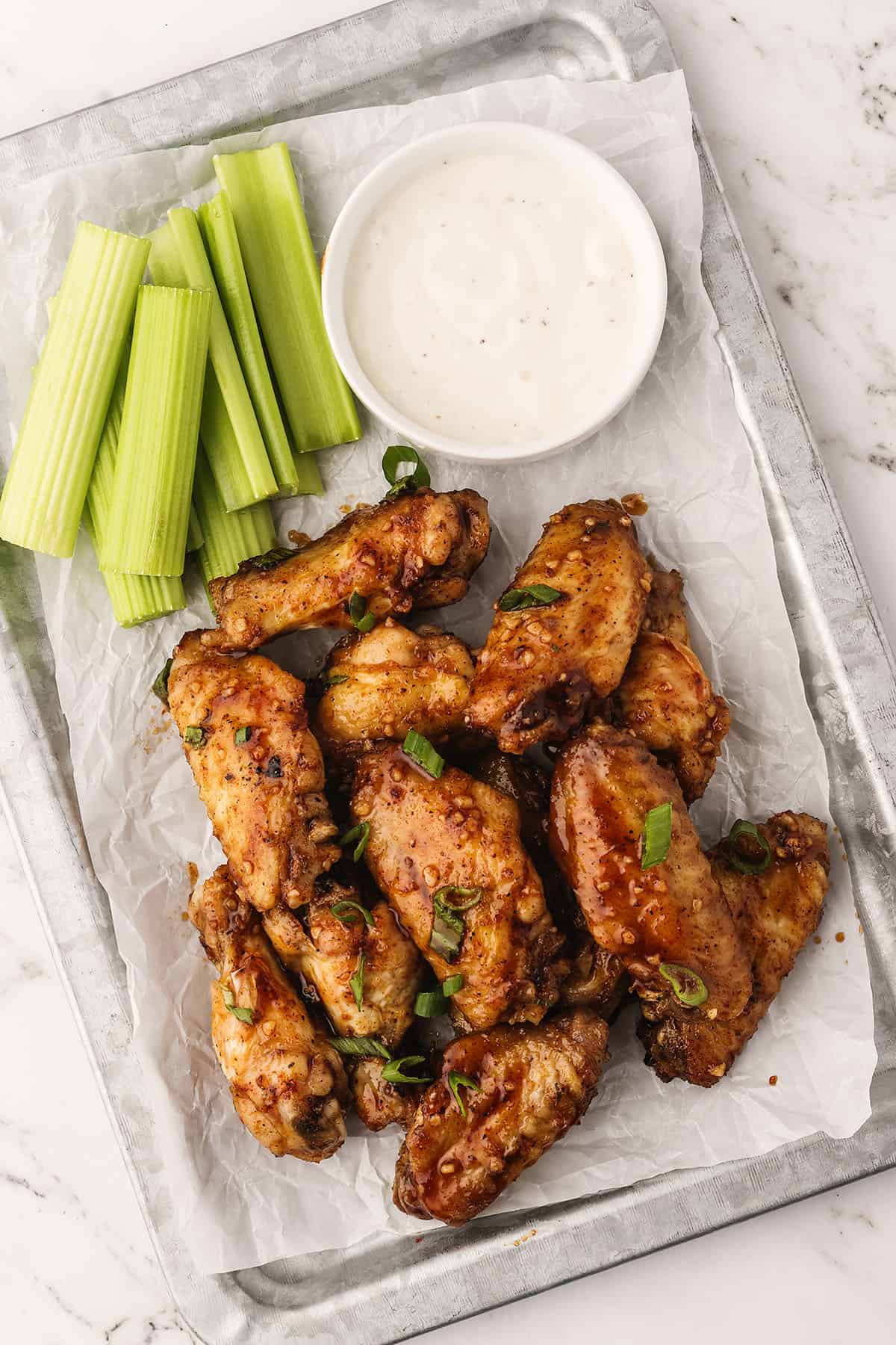 Hot honey chicken wings on metal platter with celery and ranch.