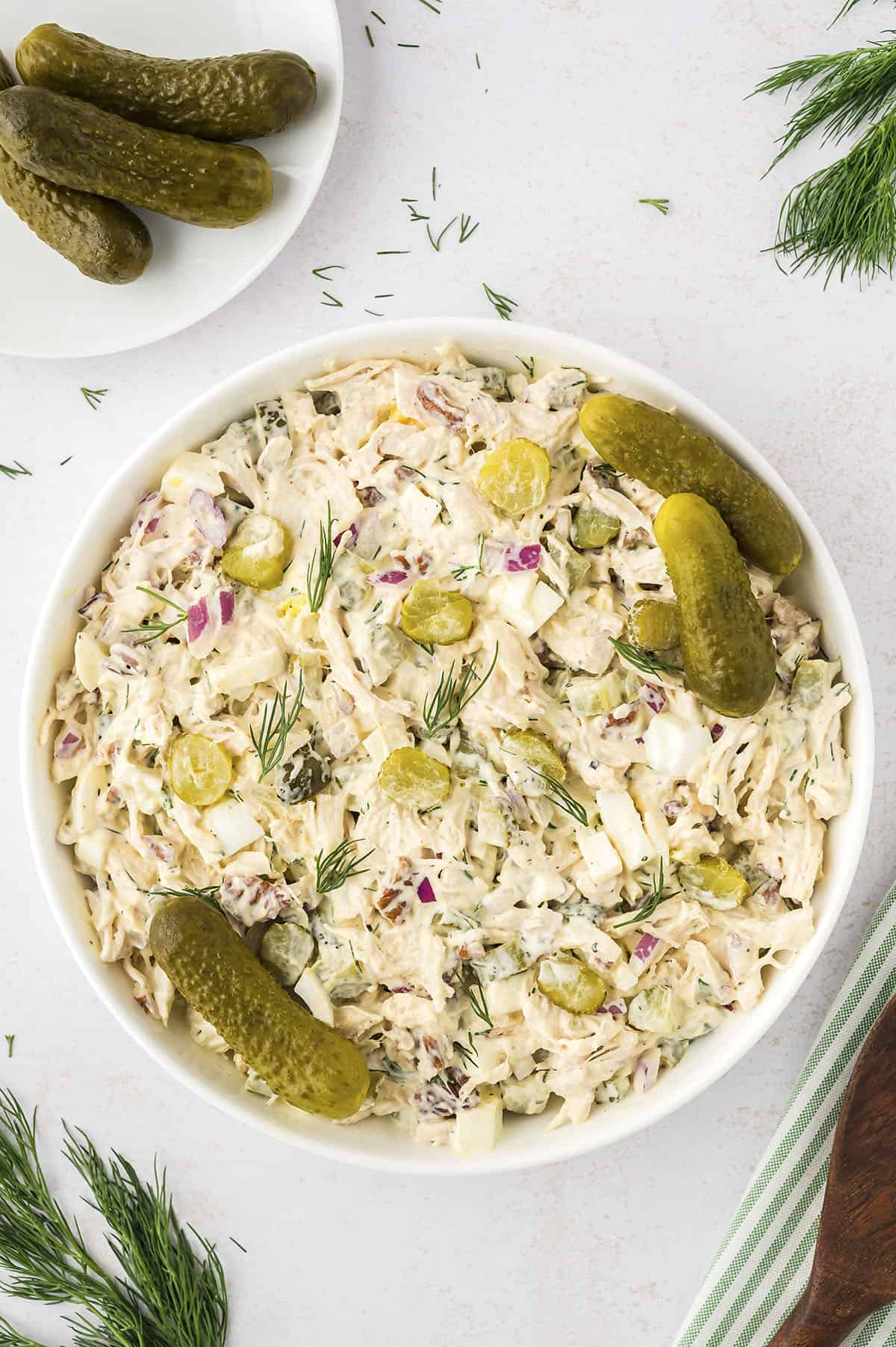 Chicken salad topped with dill pickles in white bowl.