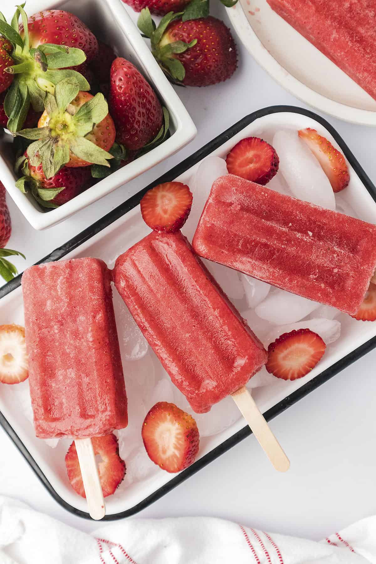 Strawberry popsicles in dish full of ice.