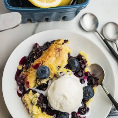 Overhead view of lemon blueberry dump cake on white plate topped with vanilla ice cream.