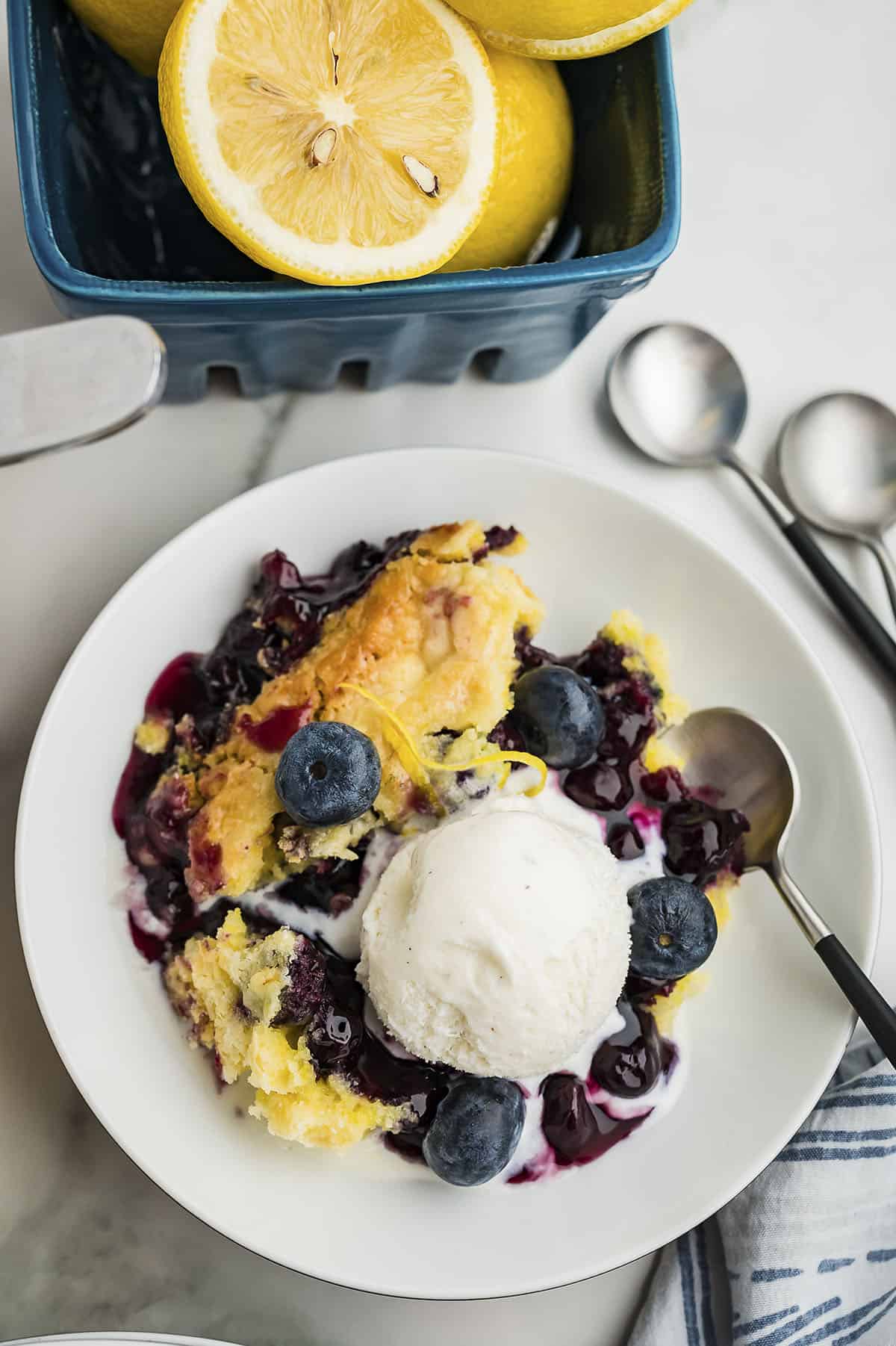 Overhead view of lemon blueberry dump cake on white plate topped with vanilla ice cream.