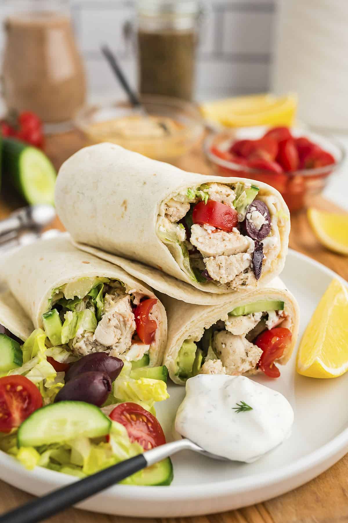 Stack of Greek chicken wraps on white platter.