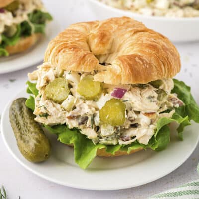 Chicken salad croissant sandwich on plate with pickle.