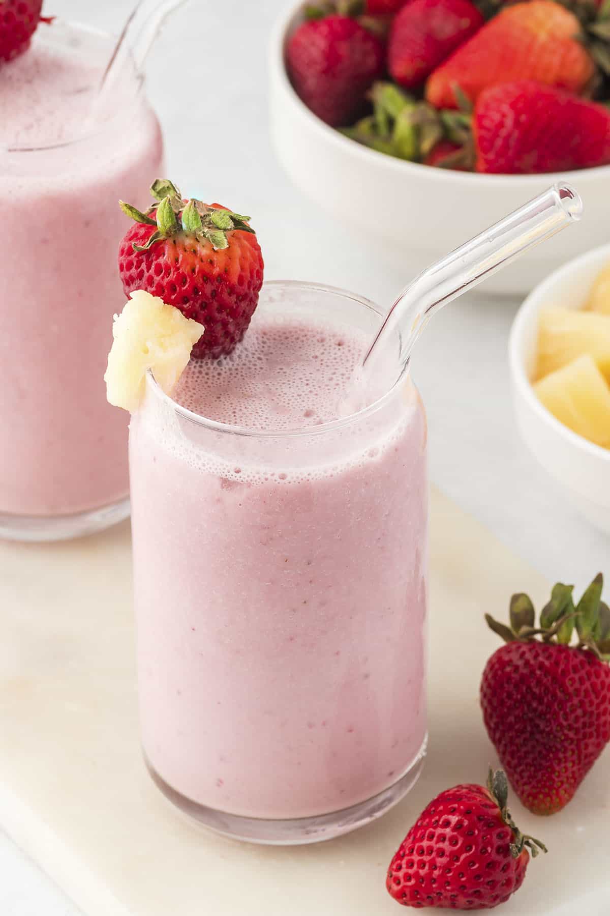 Strawberry pineapple smoothie in glass with glass straw.