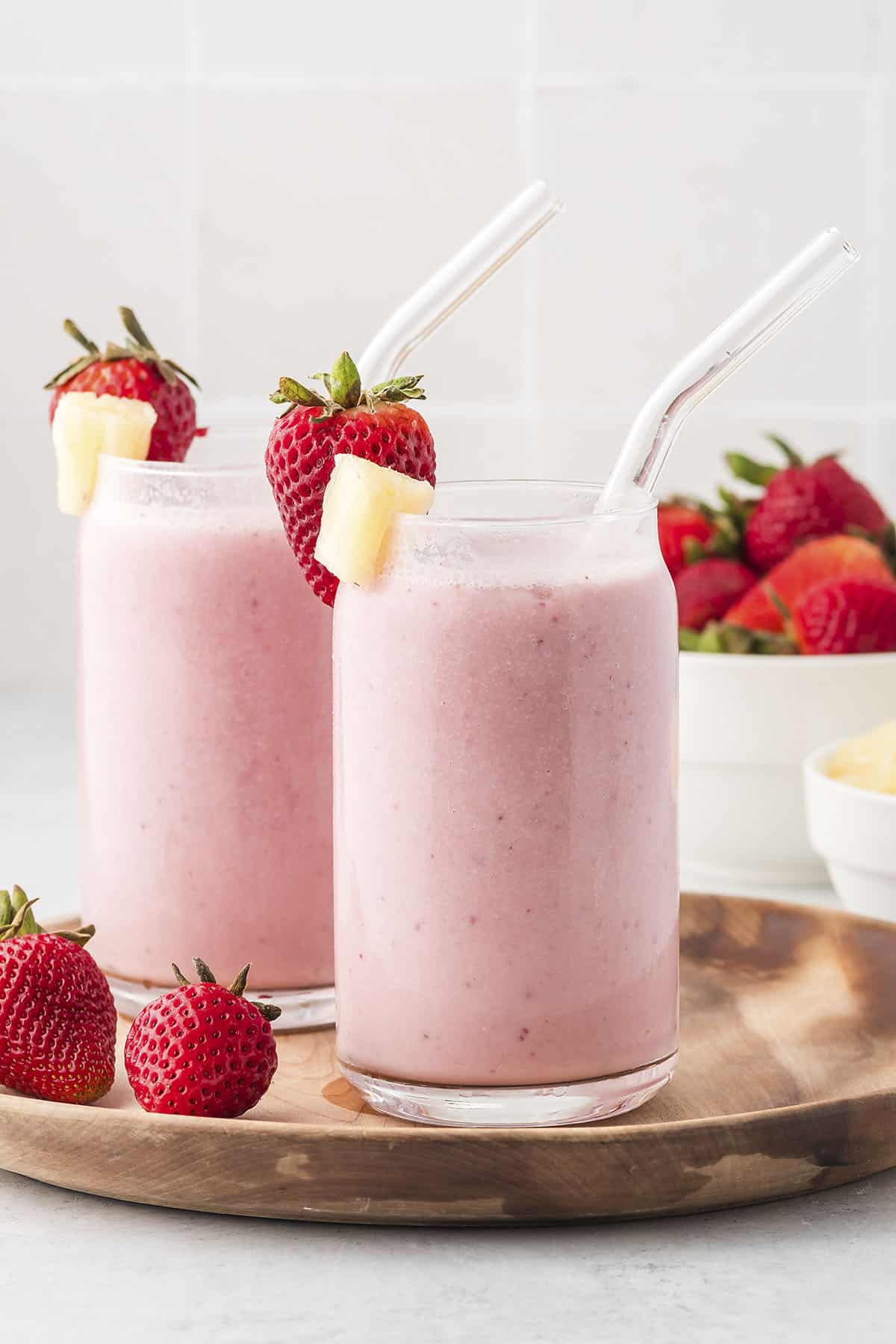 Strawberry pineapple smoothies in glasses on wooden tray.