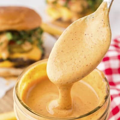 Smash burger sauce dripping off spoon into mason jar.