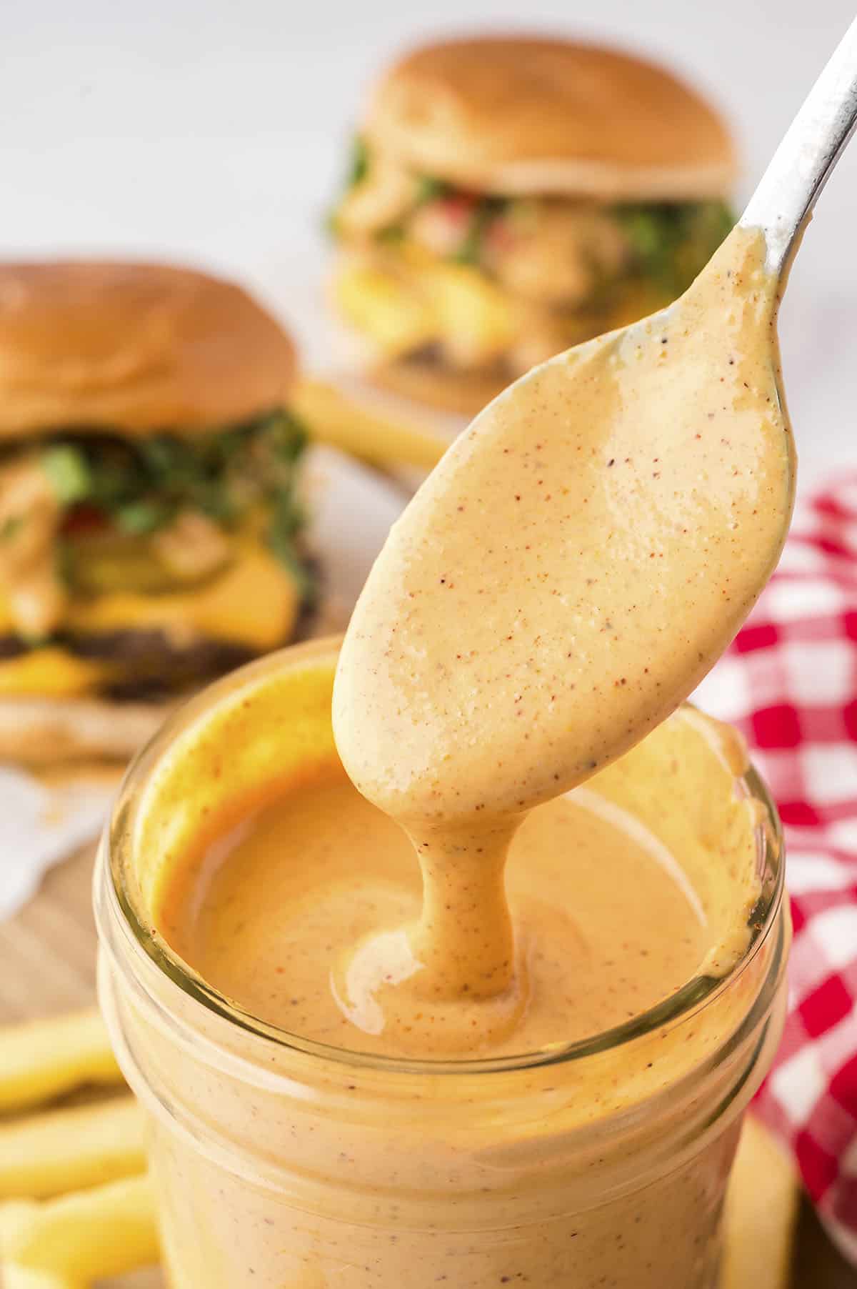 Smash burger sauce dripping off spoon into mason jar.